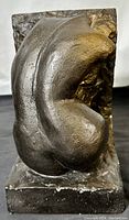 Front angled view of bronze-finished plasterware sculpture shaped as a bookend depicting seated naked woman form with textured background.