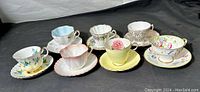 Seven bone china teacup and saucer sets displayed side by side, showing varied designs and colors.