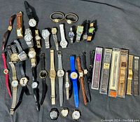Overview photo showing all watches and unopened watch bands laid out on a dark fabric surface, displaying variety and quantity.