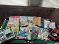 Overview of various children's books, stationery supplies, markers, and craft materials arranged on green felt surface.
