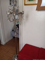 Photo of a tall silver-tone metal candelabra stand with curved arms, floral-shaped candle holders, and crystal-like dangling accents.