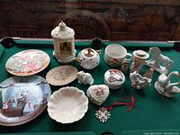 Full view of all items displayed on green pool table including plates, covered jar, teapot, various figurines, and ornament