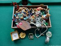 Full view of the open small box containing assorted costume jewelry, including the seller noted 18k gold filled ring in a small presentation box, multiple beaded necklaces, charm bracelets, pearl bracelet, a wristwatch, and various earrings.
