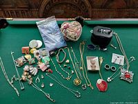 Photo showing assortment of costume jewelry including necklaces, rings, brooches, sunglasses, decorative boxes, and collectible pins.