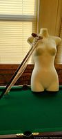 Photo showing a white female torso dress form mannequin on green surface with a wooden cane resting against it.