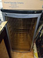 Photo of Haier wine fridge showing glass door, metal wire shelving interior, and control panel with digital temperature display at top front.