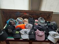 Photo of a table covered with 17 different baseball caps showing a variety of colors, logos, and brands including sports teams and commercial brands.
