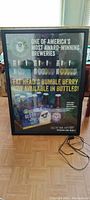 Large rectangular black framed beer sign with colorful graphics for Fat Head's Bumble Berry beer, positioned on floor in front of window. Power cord included but adapter missing.