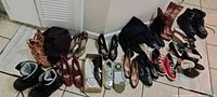 The photo shows a large lot of various women's and men's shoes and boots arranged on the floor. Styles include high heels, ankle boots, casual shoes, and sneakers in different colors such as black, brown, red, beige, and white.