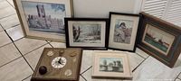 Photo showing 6 framed pictures and 1 framed wooden clock art piece arranged on tiled floor.