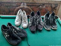 Photo of four pairs of men's sneakers in various colors, mostly black and white, placed on a green felt pool table.