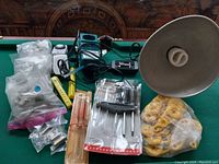 Overview photo showing all items on a green surface including the lamp reflector, Makita charger, screwdriver set, bagged yellow plastic rings, and bags of hardware pieces.