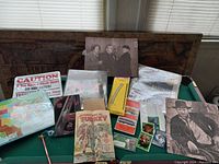 Wide view of lot on pool table showing map puzzle, caution sign, souvenir booklet, photos/posters, and various small items.