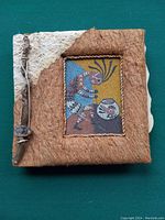 Handmade cover of the Navajo Sandpaintings book showing a textured natural material with a rectangular panel containing colorful traditional Navajo figure illustration.