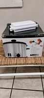 Photo showing boxed Everstar 4 quart slow cooker with microwave burger grill accessory on top.