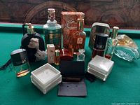 Photo of a collection of vintage perfume bottles and small storage boxes arranged on a pool table.