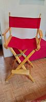 Red wooden framed director's chair with red fabric seat and backrest, shown fully assembled. Small stain on fabric is visible.