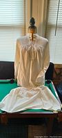 Single vintage long white night gown displayed on a dress form with visible lace neckline and pintuck details.
