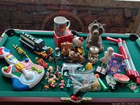 Wide shot of all vintage toys and banks laid out on a pool table with colorful musical guitar toy, train engine, ceramic animal banks, and various small figurines.