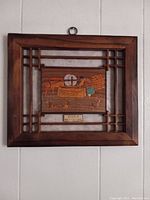 Framed wooden artwork showing entire mill stone relief with frame and plaque.