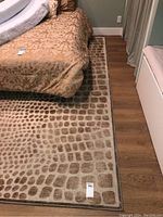 Full view of the beige and brown area rug placed in a bedroom under a bed, showing the giraffe-like pattern and overall size.