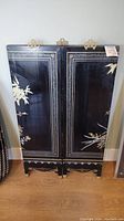 Three-panel black lacquer screen upright showing simple floral motifs painted in gold and white on the front side.