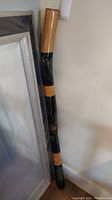 Full length view of the didgeridoo showing the black body with natural wood sections and dot painting detail.