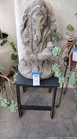 Ganesh statue seated on black wooden table with some surrounding plants.