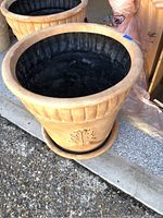 Large terracotta colored garden pot with vertical ribbing and decorative leaf motif. Matching saucer under pot visible. Interior shows use marks.