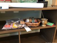 View of brass incense burner, unopened incense boxes in a basket, and a bag with matchbooks on shelf.