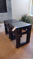 Two black lacquer Japanese occasional tables from angled side view on wooden floor, near a modern fireplace and plant.