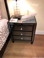 Front view showing mirrored three-drawer nightstand with crystal-like knobs and decor on top.