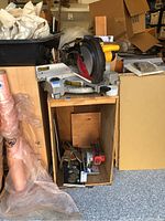 Angled front view of DeWalt miter saw mounted on wooden box with clutter around