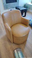 Front view of the caramel-colored swivel bucket chair showing smooth faux leather and rounded shape.