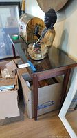 Wood table with dark finish and clear glass top, tapered legs, shown with Buddha sculpture on top and boxes underneath.