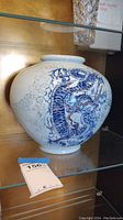 Photo of the vase showing the blue and gold handpainted dragon on white porcelain, placed on a glass shelf.