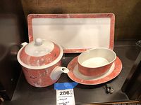 Photo showing teapot with lid, rectangular sandwich platter in background, and oval uncovered dish with underplate in foreground, all with red marble patterned rims.