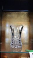 Front view of the Waterford Crystal Lismore cut crystal vase on a glass shelf with gold background, showing the shape and cut pattern.