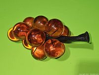 Amber lucite grape cluster with round translucent spheres on a dark brown stem lying on green background.