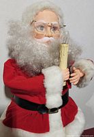 Close-up showing Santa's face with glasses and white beard, holding a candle distinctively made to appear lit.