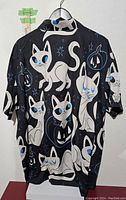 Full back view of the XXL black cat Hawaiian shirt showing multiple white cartoon cats with blue eyes on black background.