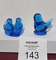 Two blue glass Bluebird of Happiness figurines on white platform, seller number 143 visible