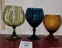 Front view of three vintage Empoli art glass snifters arranged in a row next to a rulers for height reference; distinct colors and textures visible.