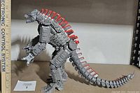 Side view of large gray plastic MechaGodzilla figure with red spines, showing articulated limbs and length with ruler for scale.