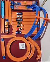 Photo of orange and blue Hotwheels track parts laid out, along with six miniature Hotwheels cars in various colors and designs. Some track parts still packaged.