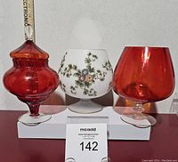 Three Italian art glass brandy snifters: one satin glass with hand paint floral design, two red Empoli style glasses, one with lid.