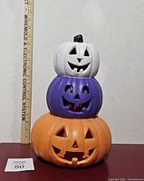 Front view of the Jack O Lantern totem showing three stacked pumpkins in white, purple, and orange colors with carved faces.