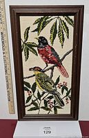 Full view of framed needlepoint with two colorful birds on branches and leafy background.