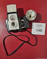 Vintage Brownie Starflex twin lens reflex camera with attached flash on red background, showing front and side with strap.