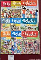 Front view of nine Highlights for Children magazines arranged in three rows, showing colorful illustrated covers with various scenes from the 1980s